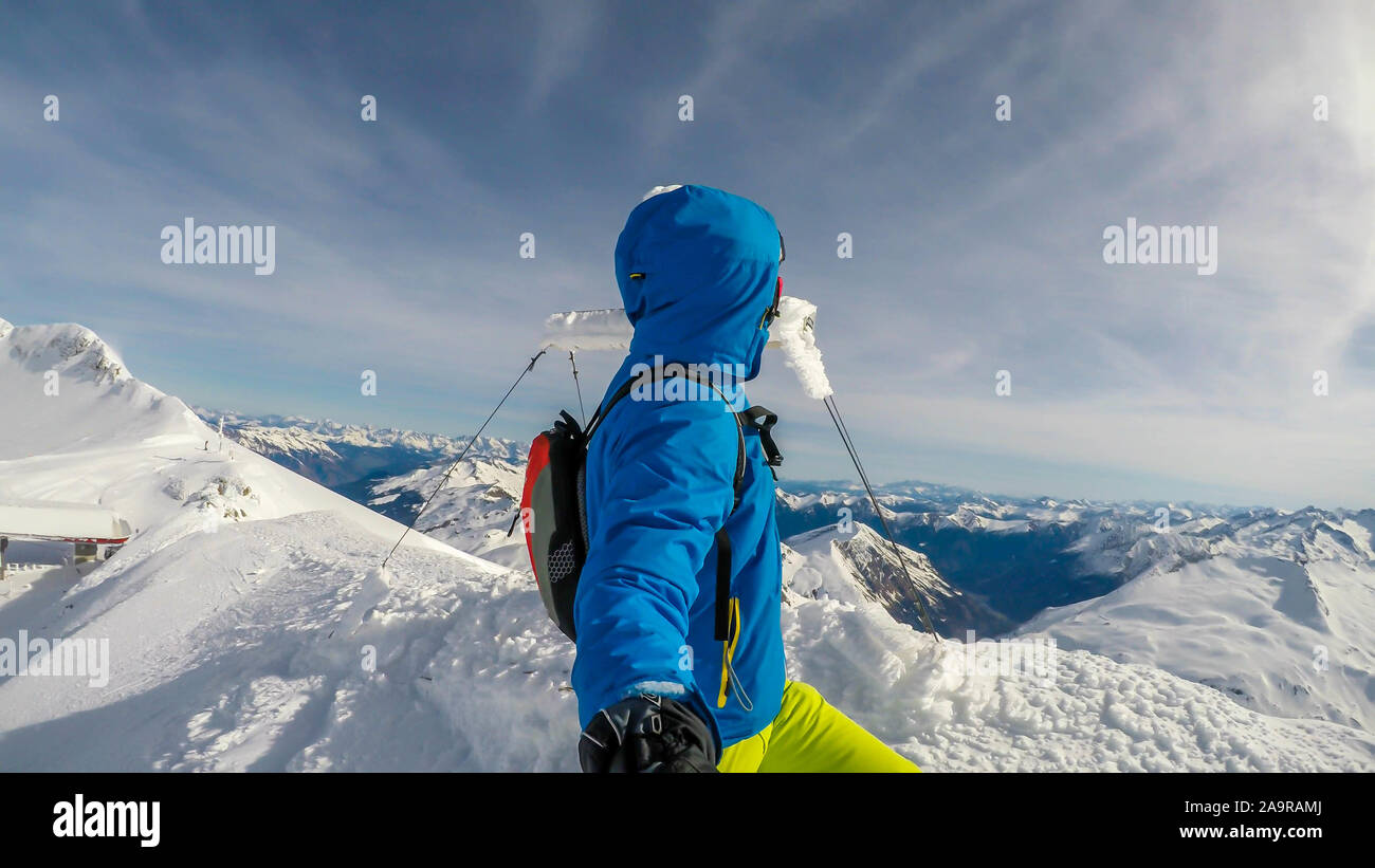 Un uomo in abito di sci in piedi sulla cima di una montagna con una coperta di neve croce dietro di lui. Infinite tappata da neve montagne intorno all'uomo. Soft Foto Stock