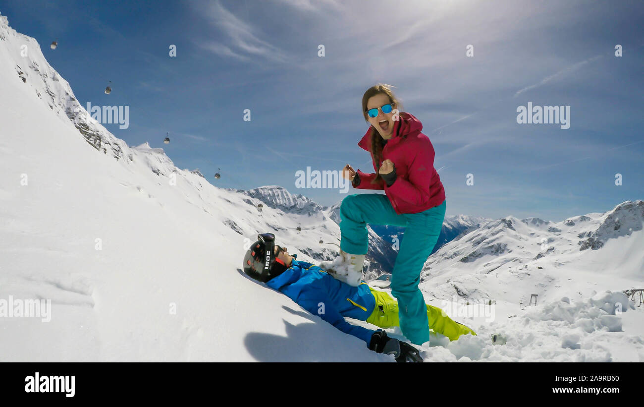 Un paio di sci outfits giocando nella polvere di neve. La ragazza è in piedi con un piede sul ragazzo, come se lei lo ha battuto. Lei è felice e trionfante. Fine Foto Stock