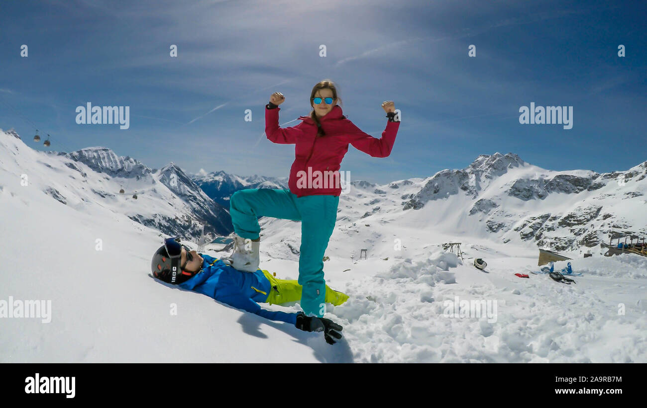 Un paio di sci outfits giocando nella polvere di neve. La ragazza è in piedi con un piede sul ragazzo, come se lei lo ha battuto. Lei è felice e trionfante. Fine Foto Stock