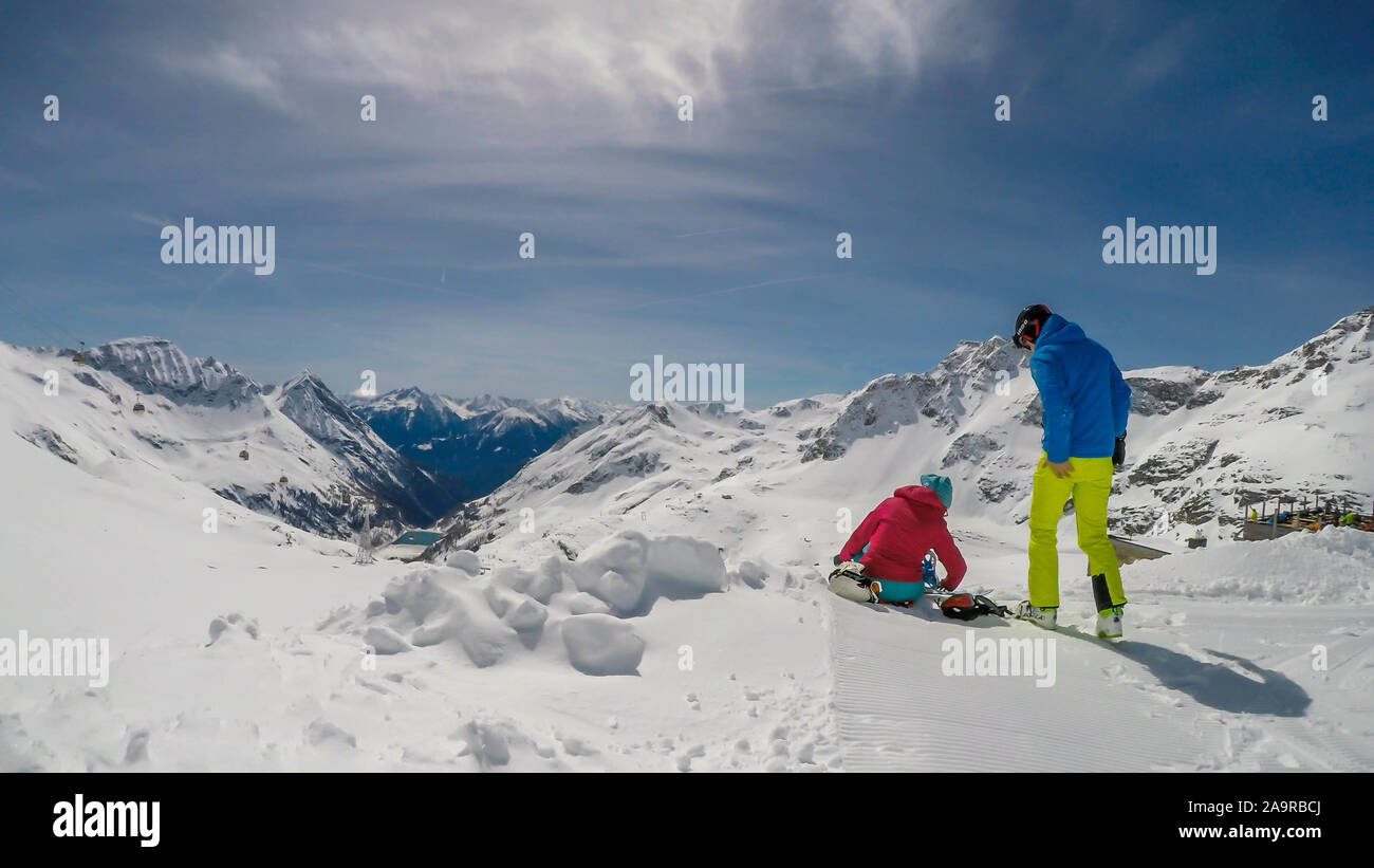 Un paio di sci abiti, seduto sulla neve e godere la montagna innevata. Infinite gamme di neve montagne tappata davanti a loro. Togethernes Foto Stock
