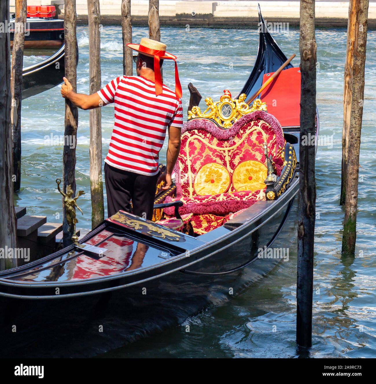 Venezia, Italia. Gondoliere in una striata maglietta rossa e il cappello in  una gondola ormeggiata sul canale Foto stock - Alamy