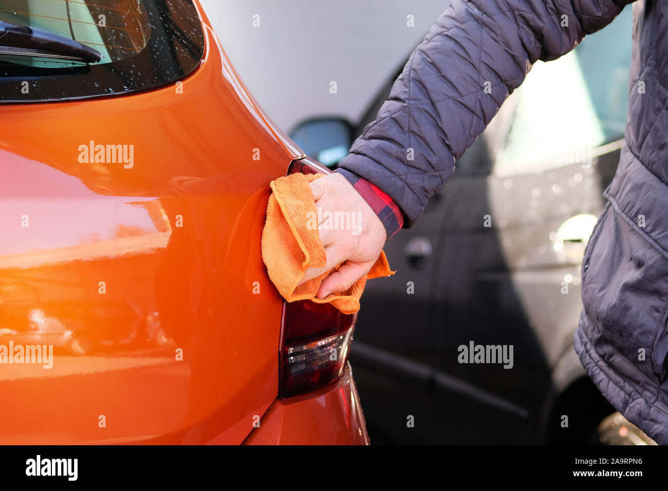 L'uomo dopo salviette per la pulizia la sua vettura arancione con uno straccio al car wash. Mano maschio e la carrozzeria di auto closeup. Foto Stock