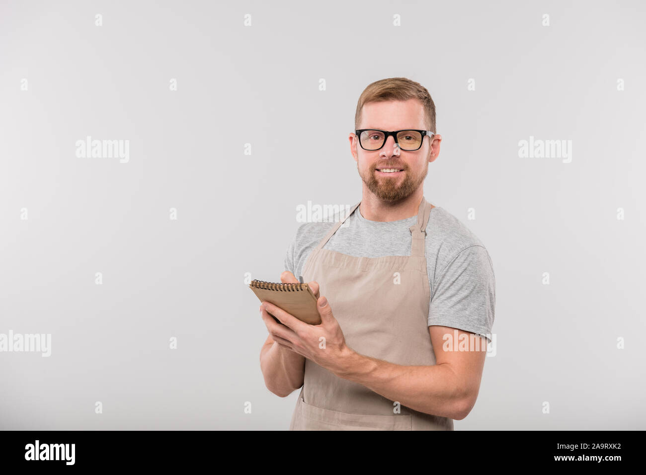 Felice giovane cameriere barbuto iscritto all ordine del cliente in Blocco note Foto Stock