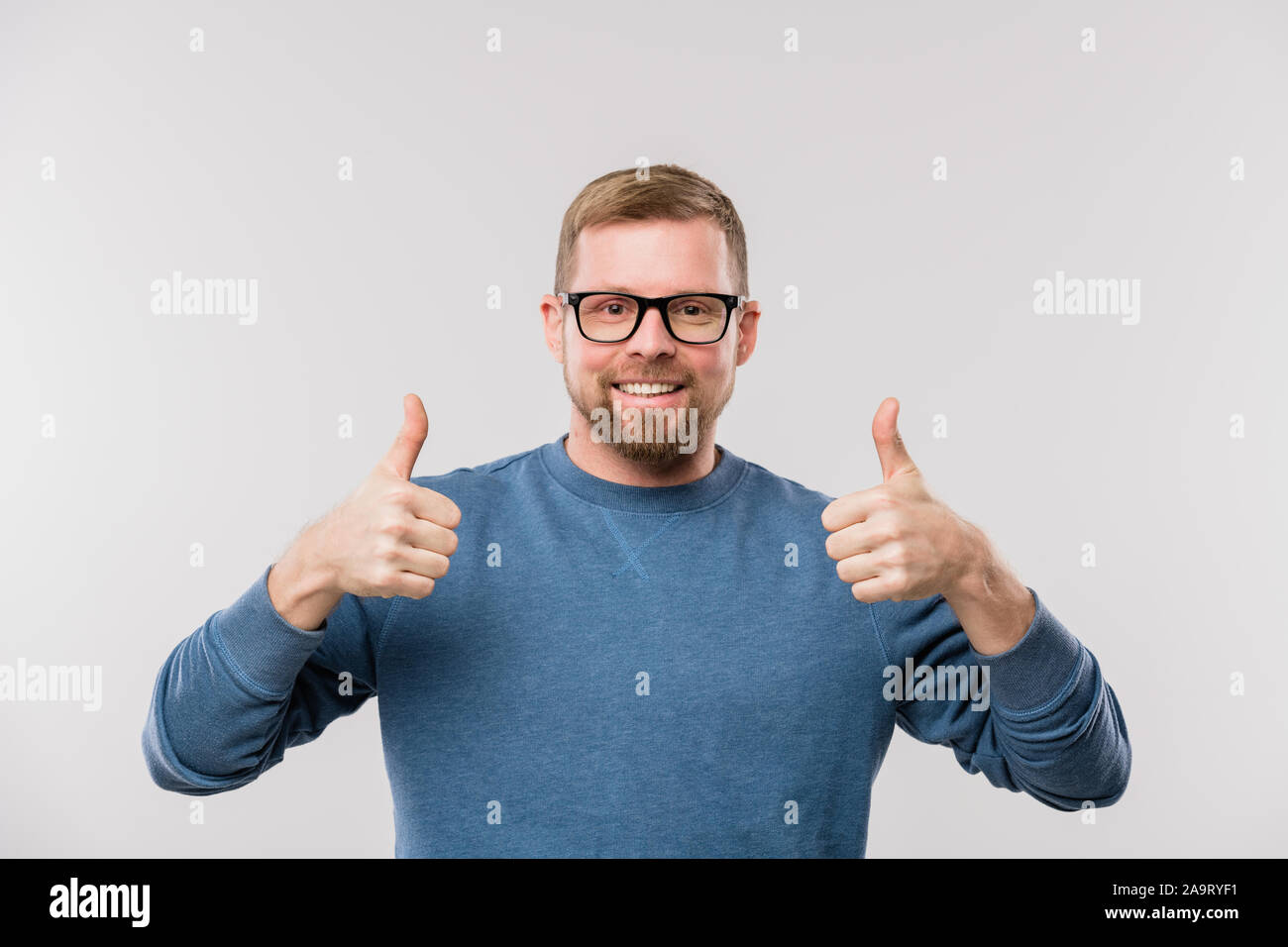 Giovane imprenditore allegro in maglia blu che mostra i pollici fino in isolamento Foto Stock