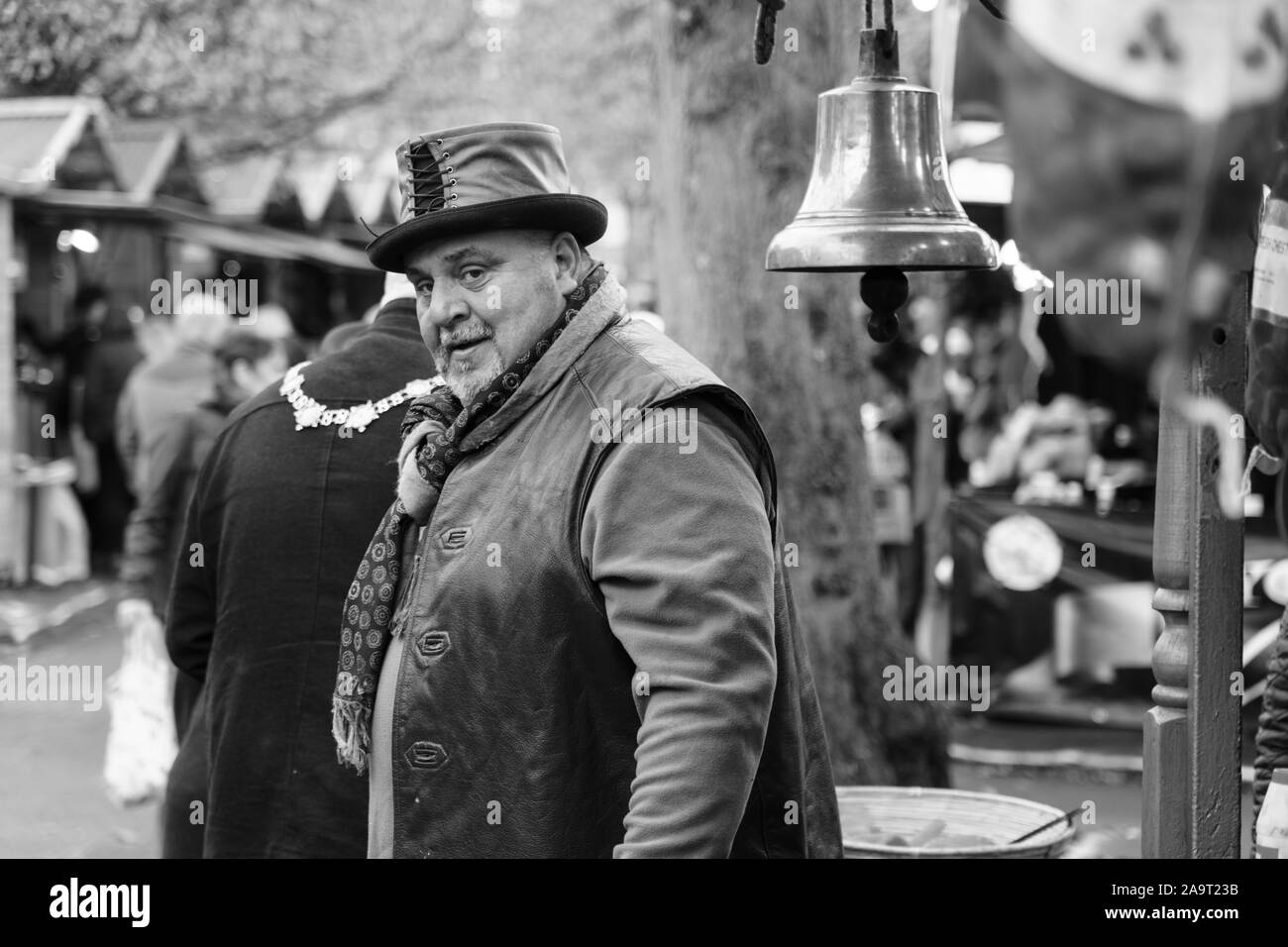 Male Market Trader che indossa un gilet e un cappello in pelle che vende nocciole a cavallo caldo al mercato di Natale di Harrogate, North Yorkshire, Inghilterra, Regno Unito. Foto Stock
