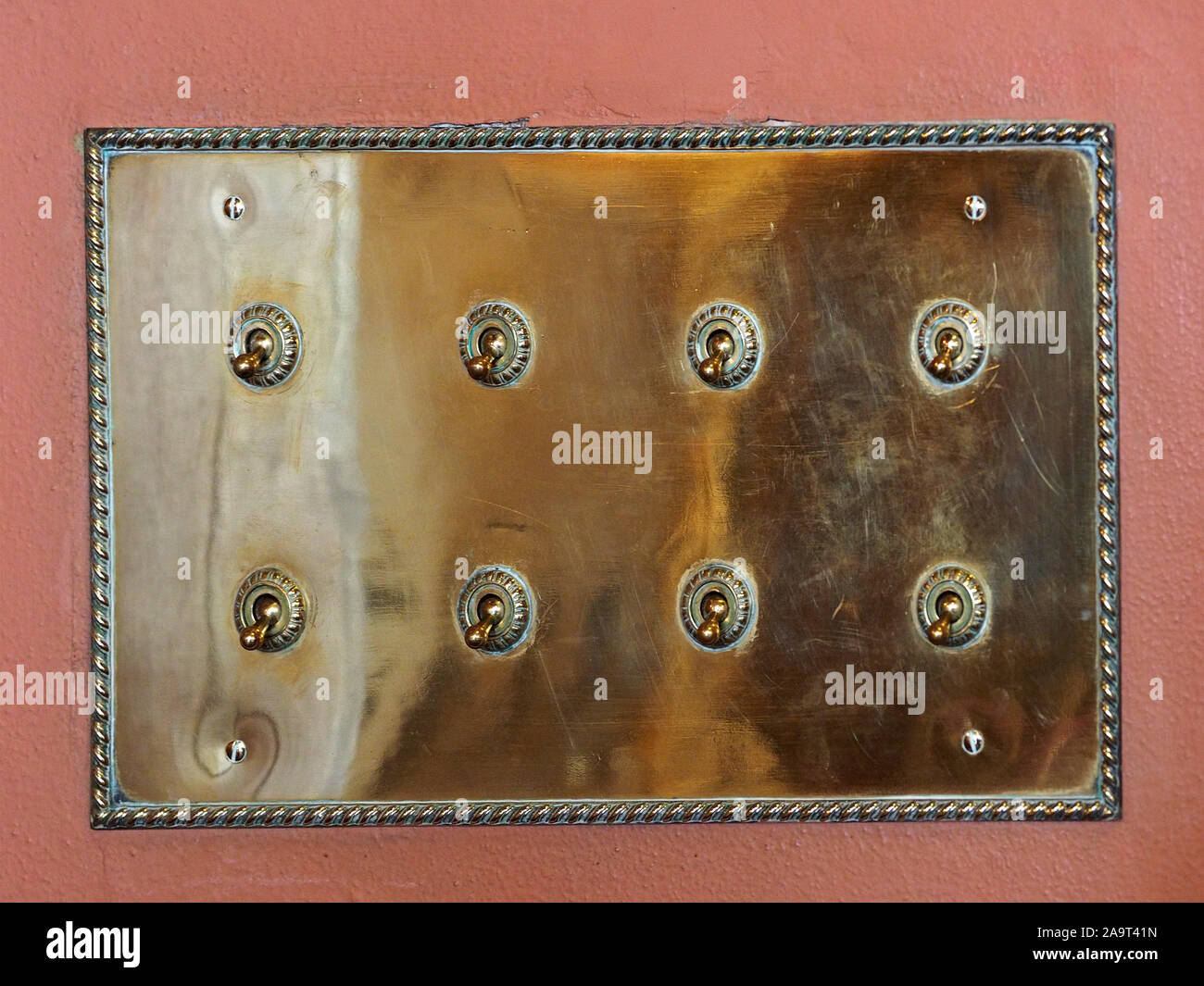 Ottone lucido switch-piastra con otto in vecchio stile interruttori elettrici su rusty ocra parete dipinta nella storica casa in Inghilterra, Regno Unito Foto Stock