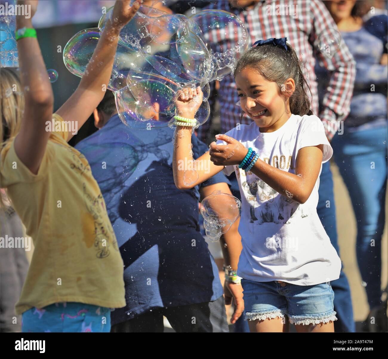 Ispanico messicano latina i bambini, i ragazzi e le ragazze a caccia di bolle dal circo fair act fatta con acqua e sapone per pubblico spettacolo e divertimento per tutta la famiglia Foto Stock