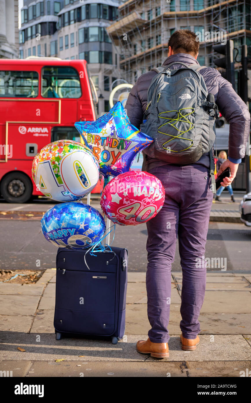 L'uomo visto da dietro, la laminazione di una valigia con il quarantesimo compleanno palloncini attaccata alla maniglia Foto Stock