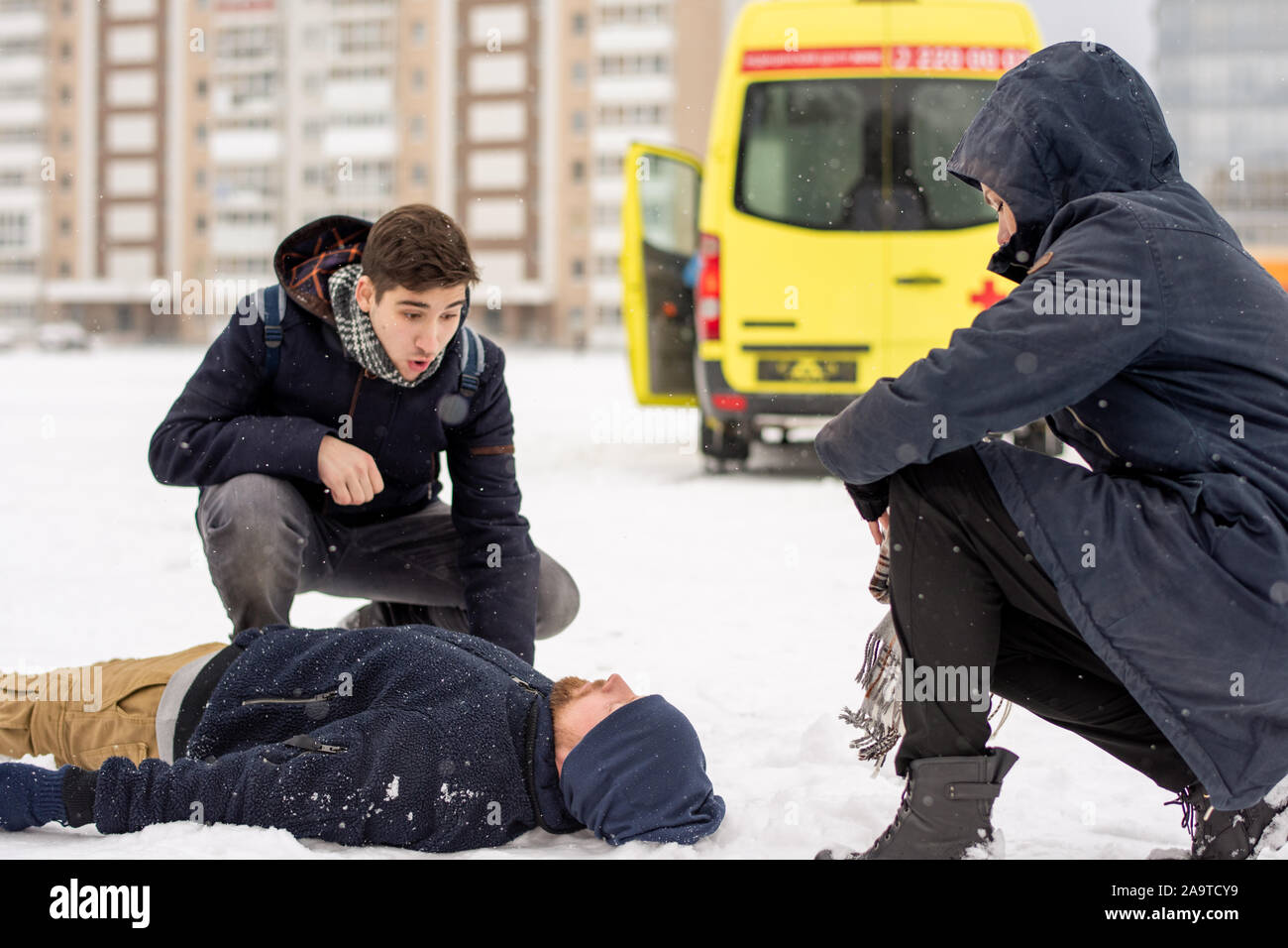 Due persone sedute su squat da malati o in stato di incoscienza giovane uomo disteso nella neve Foto Stock