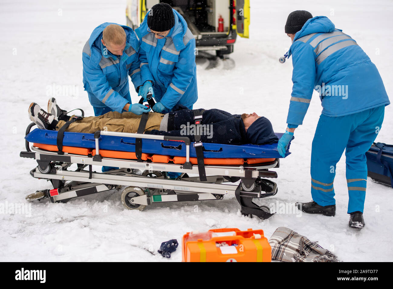 Due giovani paramedici nel fissaggio di indumenti da lavoro per uomo incosciente con cinghie sulla barella Foto Stock