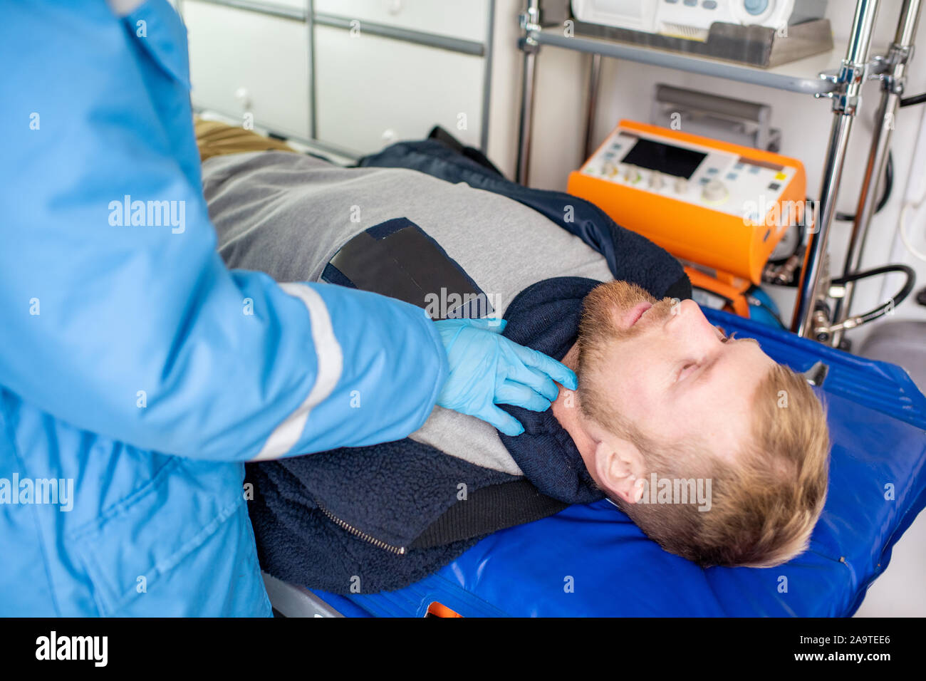 La mano guantata di personale paramedico cheking impulso di malati uomo disteso sulla barella Foto Stock