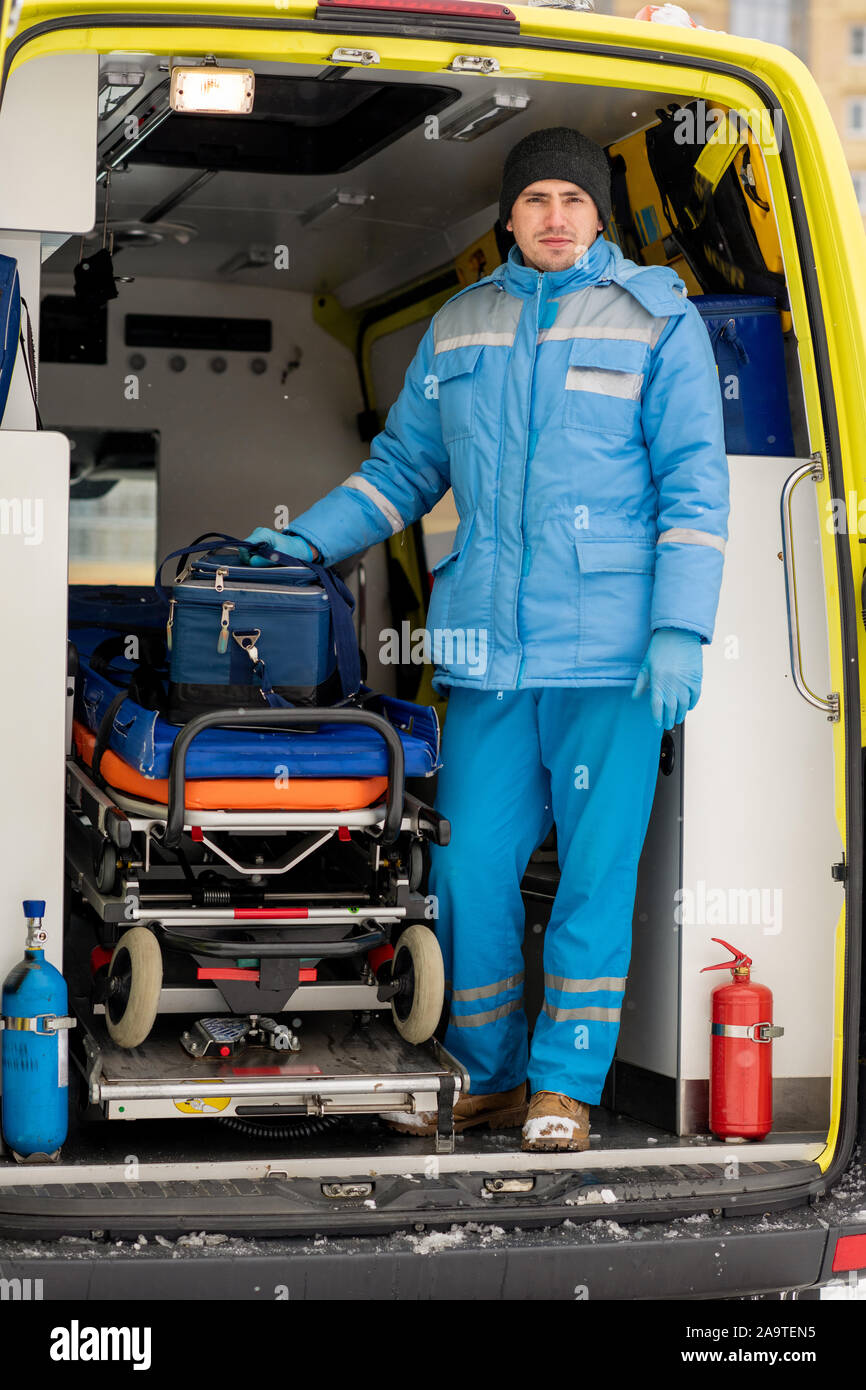 Giovane paramedico con kit di primo soccorso in piedi da barella all'interno di ambulanza Foto Stock