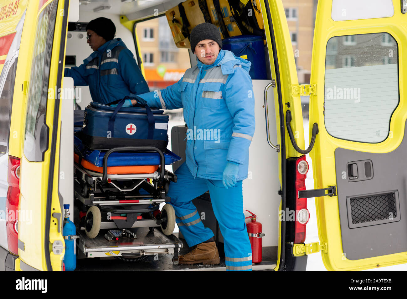Paramedico maschio con kit di primo soccorso in piedi da barella in ambulanza Foto Stock