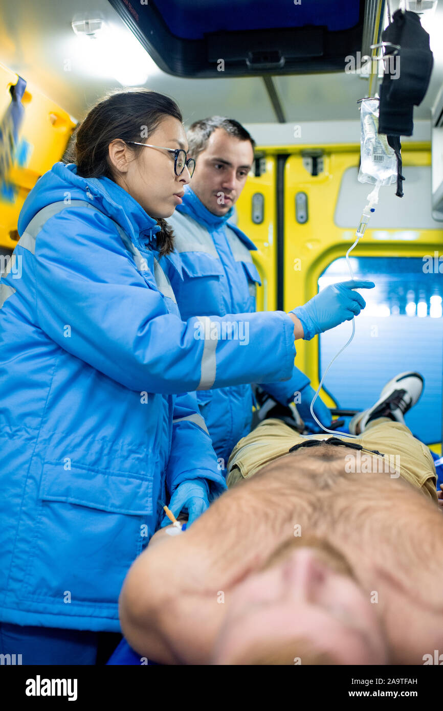 Due giovani paramedici preparare un contagocce per uomo malato all'interno di ambulanza Foto Stock