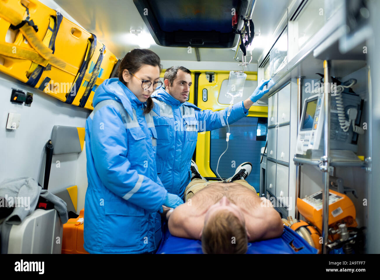 Paramedic esaminando uomo malato sulla barella mentre il suo collega la preparazione di un contagocce Foto Stock