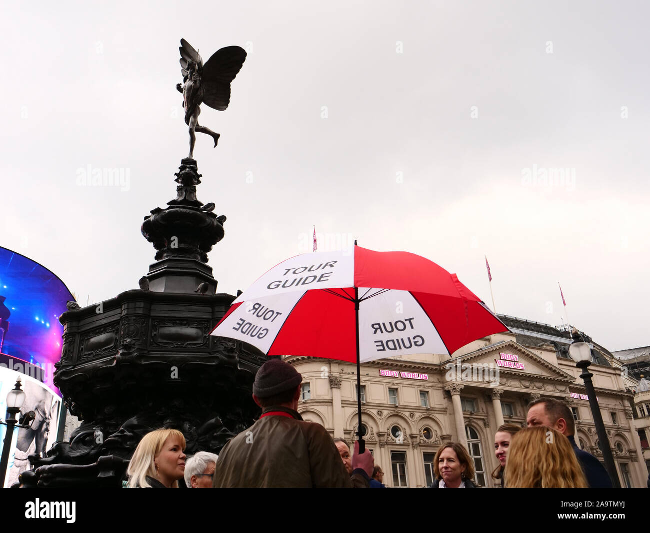 Tour con guida di colore rosso e bianco ombrello visto con un gruppo di turisti a Piccadilly Circus a Londra, Inghilterra, Regno Unito nel novembre 2019. Foto Stock