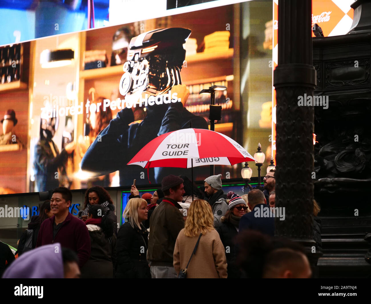 Tour con guida di colore rosso e bianco ombrello visto con un gruppo di turisti a Piccadilly Circus a Londra, Inghilterra, Regno Unito nel novembre 2019. Foto Stock