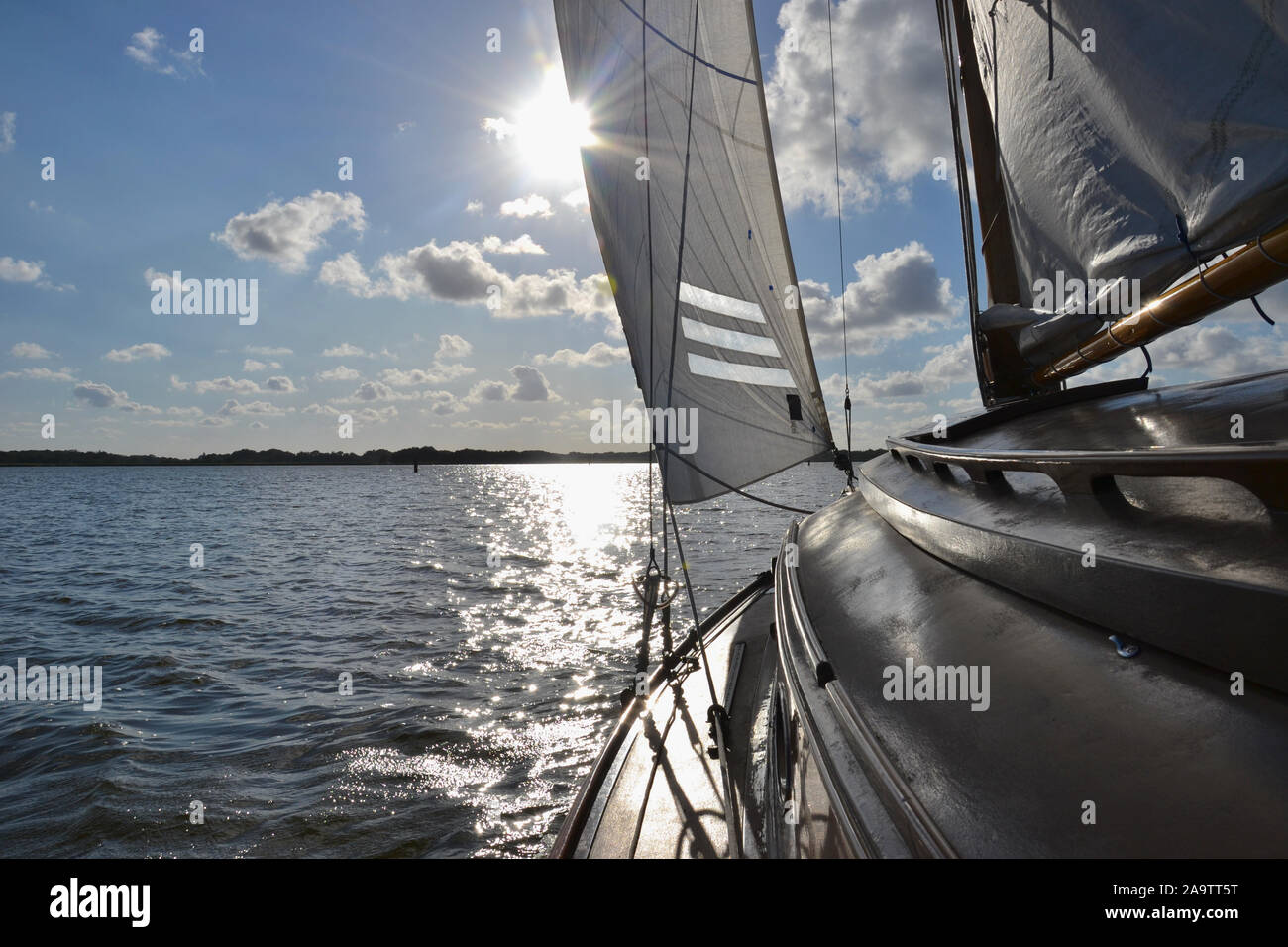 Parte superiore della cabina e il braccio su un tradizionale in legno yacht a vela, vela verso il sole su un ampio lago nel Norfolk Broads (UK). La luce del sole scintillante sul Foto Stock