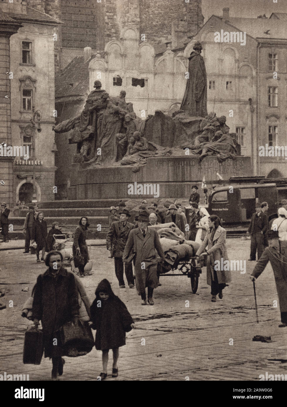 I rifugiati tedeschi con i loro averi davanti al monumento a Jan Hus in Piazza della Città Vecchia di Praga, Cecoslovacchia, nel maggio 1945. Fotografia in bianco e nero dal fotografo ceco Stanislav Hulík pubblicato nel libro cecoslovacca 'Memory Libro della insurrezione di Praga' ('Památník Pražského povstání") rilasciata nel 1946. La fotografia è stata probabilmente preso nel pomeriggio del 8 maggio 1945, quando la popolazione tedesca di Praga è stata in grado di lasciare la città dopo la capitolazione del presidio tedesco dopo l'insurrezione di Praga. La Casa alla Campana di pietra (Dům u Kamenného zvonu) prima del restauro Foto Stock