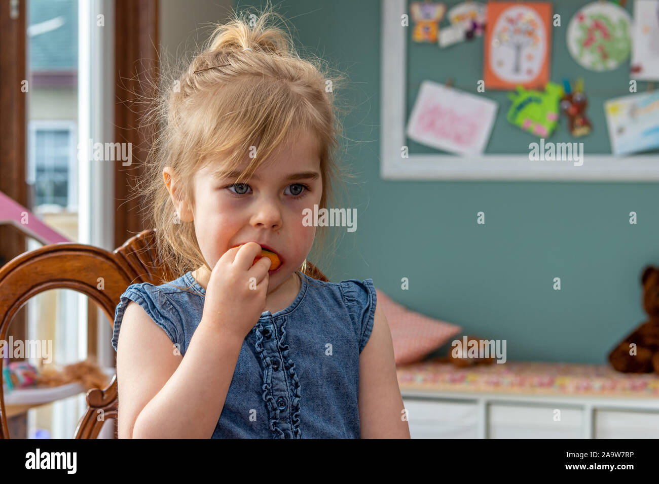 Molto carino giovane ragazza, con abbastanza occhi blu, seduto al tavolo della cucina di mangiare un arancio. Foto Stock