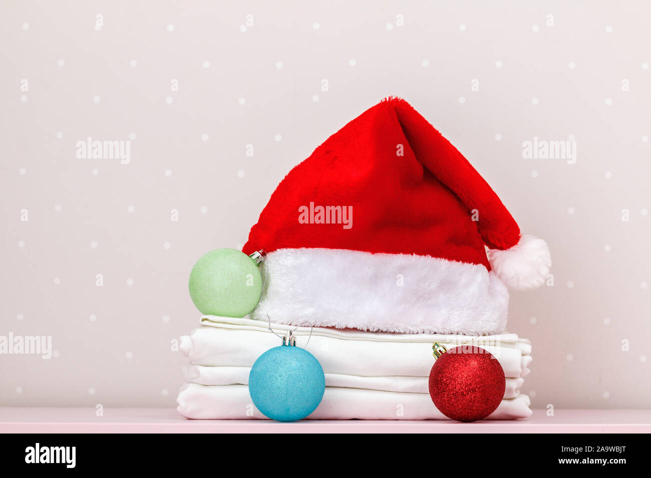 Primo piano di una pila di biancheria da letto pulita e una Santa Claus hat, palle di Natale in una tabella sullo sfondo di una parete di luce. Foto Stock