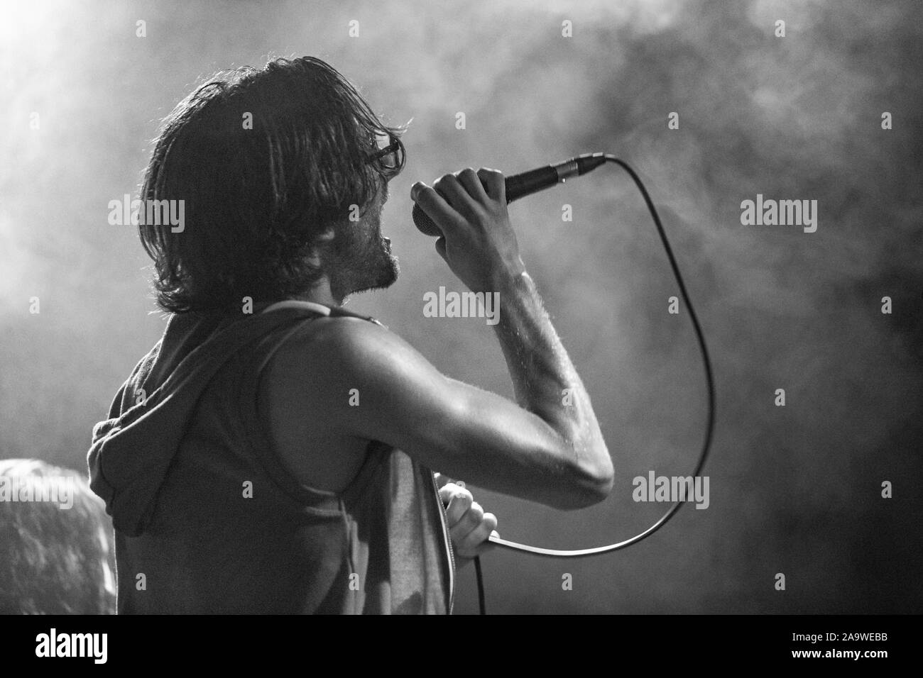Un musicista maschio è visto dal lato come canta, con bocca aperta nel microfono e interagisce con il pubblico, in bianco e nero con spazio di copia Foto Stock