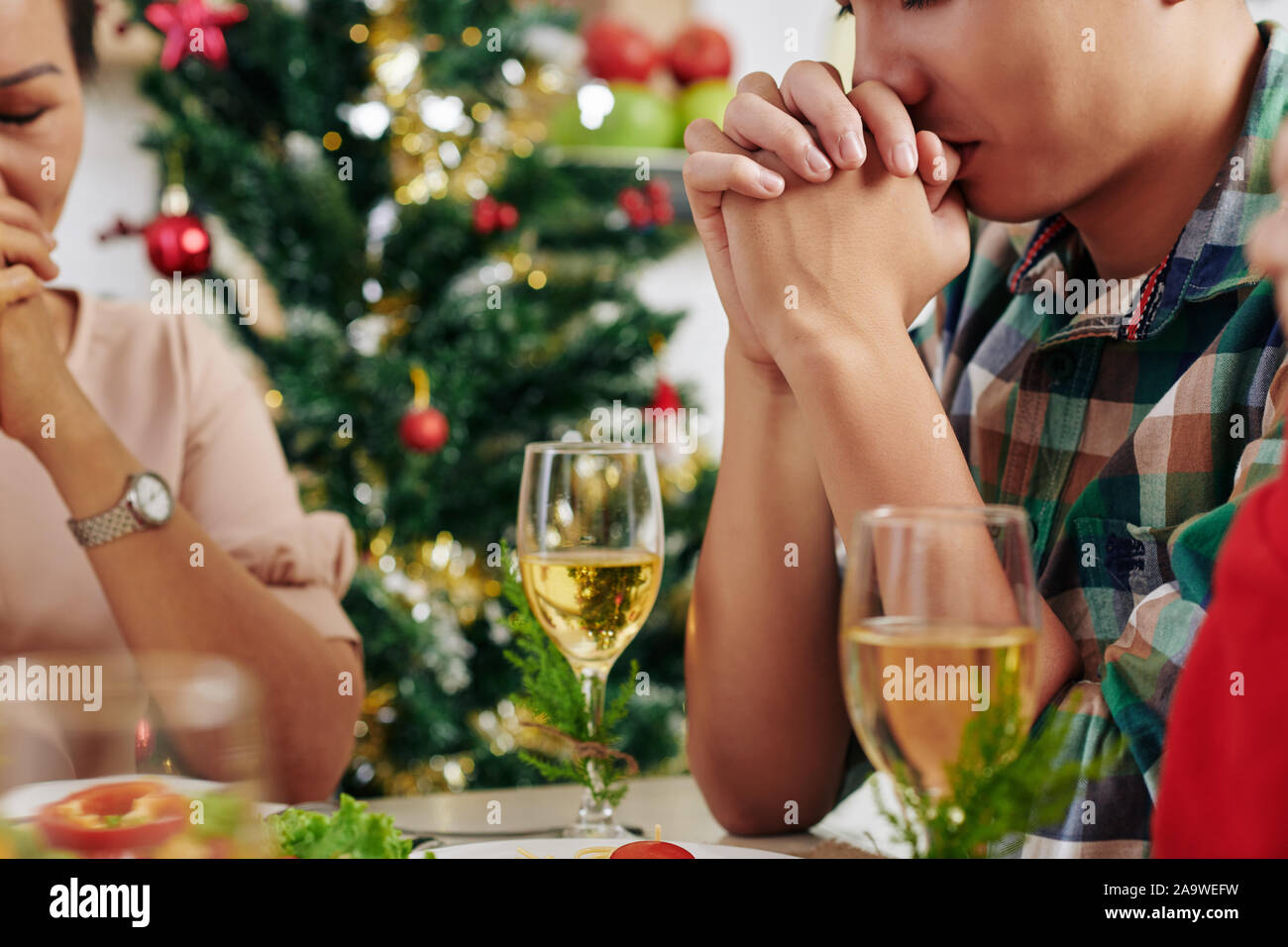 Immagine ritagliata di persone in preghiera prima di mangiare la cena di Natale a casa Foto Stock