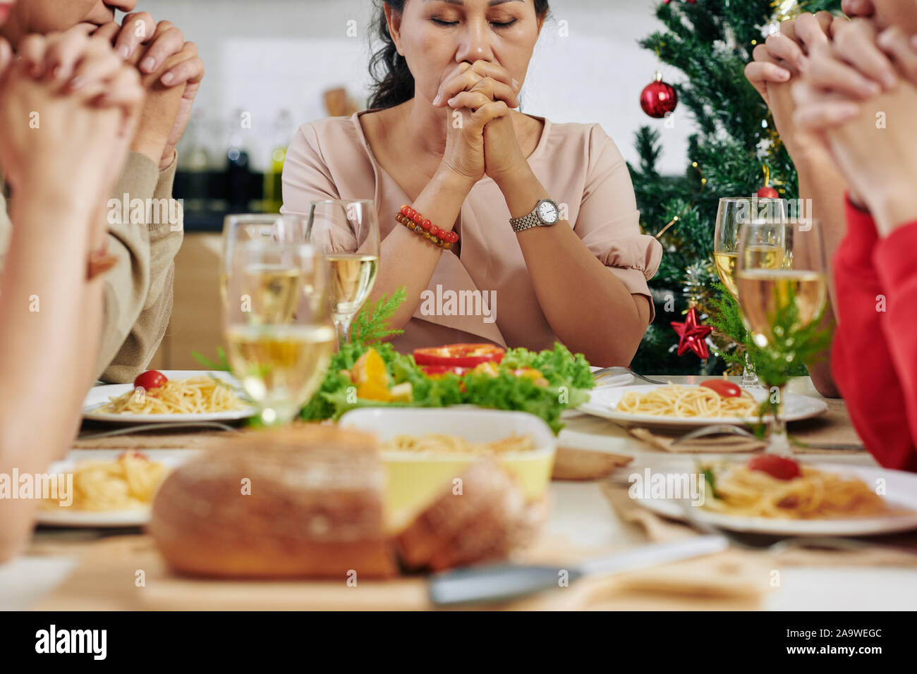 Grande famiglia asiatica di chiudere gli occhi e pregare prima di mangiare la cena della vigilia di Natale Foto Stock