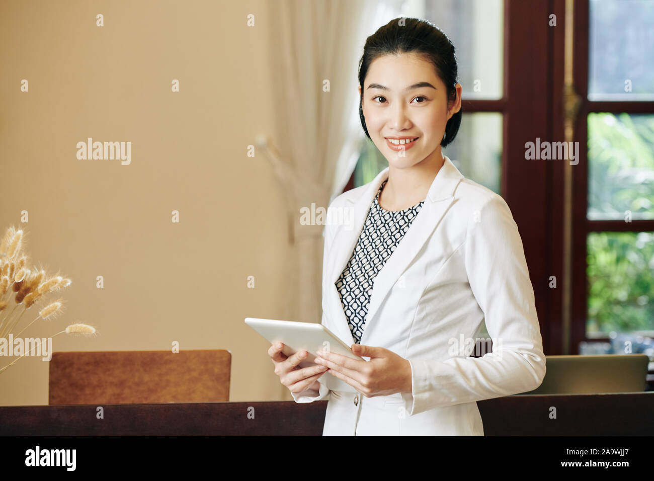 Giovane bella spa salon receptionist in piedi presso il luogo di lavoro con computer tablet in mani Foto Stock