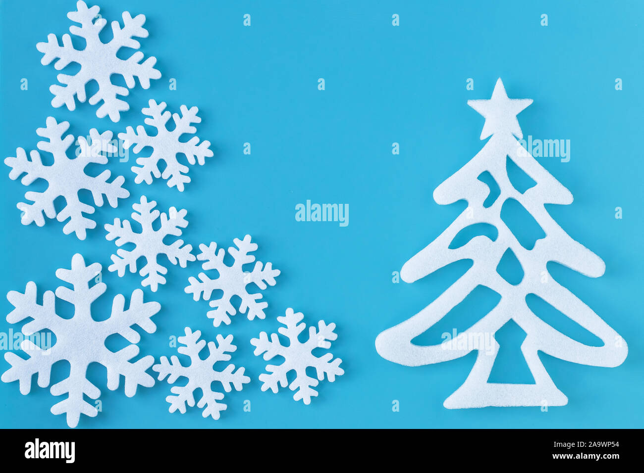 Applique di carta bianca con fiocchi di neve intagliati e albero di natale su sfondo blu. Cartolina di stile minimalista. Anno nuovo layout fatti a mano. Foto Stock