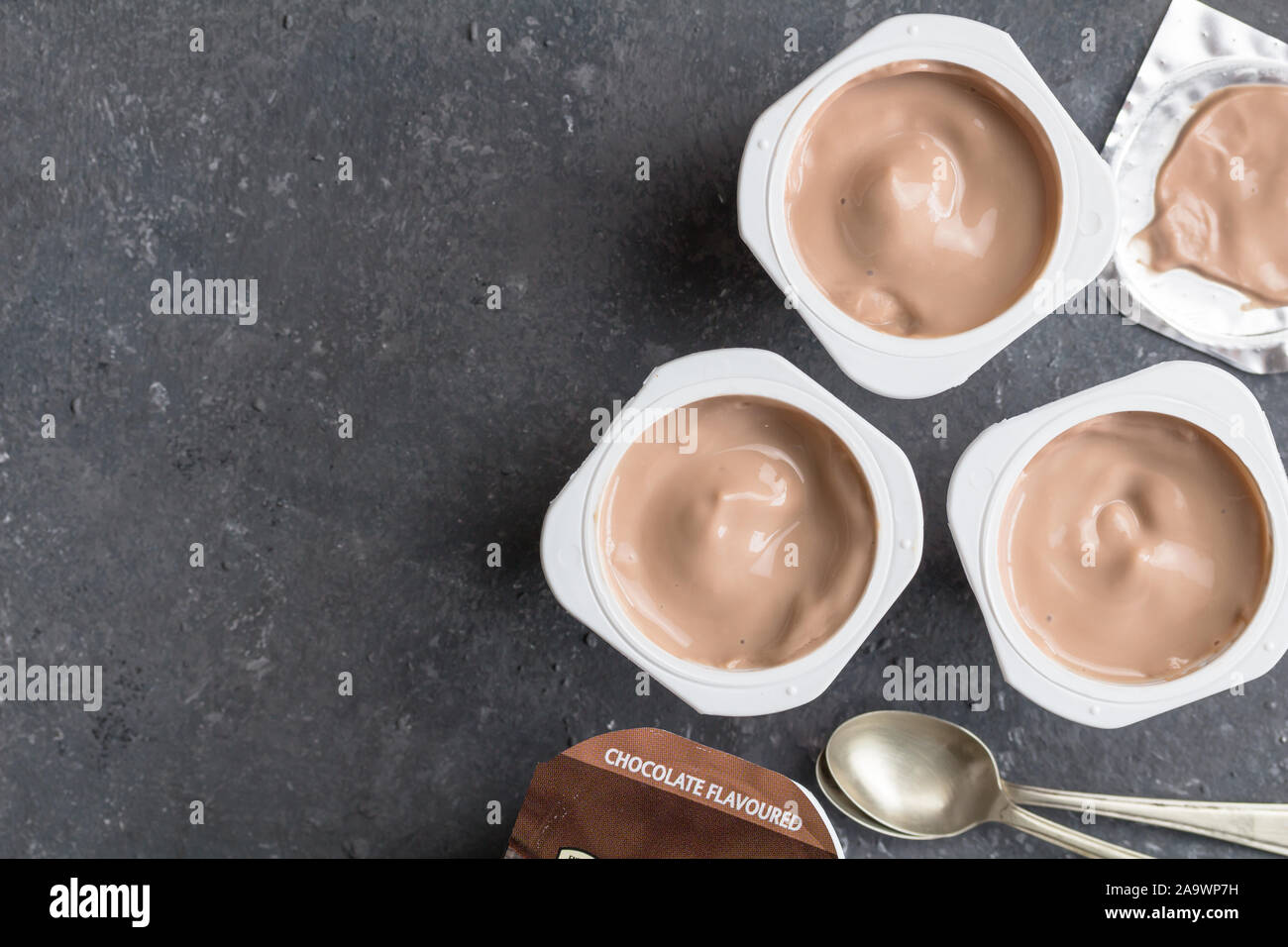 Il cioccolato vasetti per yogurt nero su sfondo a chiazze con piccoli cucchiai di argento - Tre aromatizzato al cioccolato yogurt bicchieri con coperchio di lamina Foto Stock