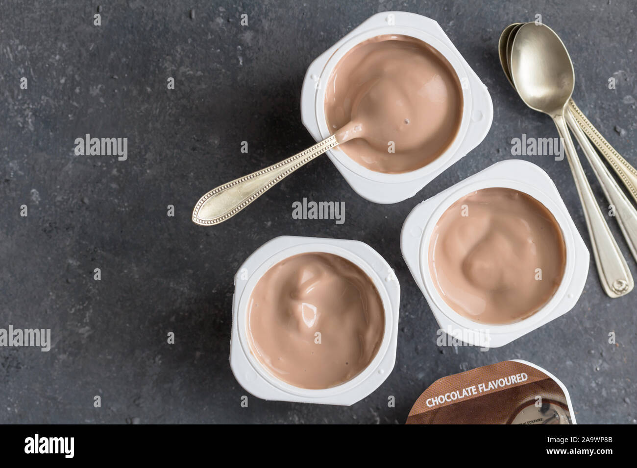 Il cioccolato vasetti per yogurt nero su sfondo a chiazze con piccoli cucchiai di argento - Tre aromatizzato al cioccolato coppe di yogurt Foto Stock