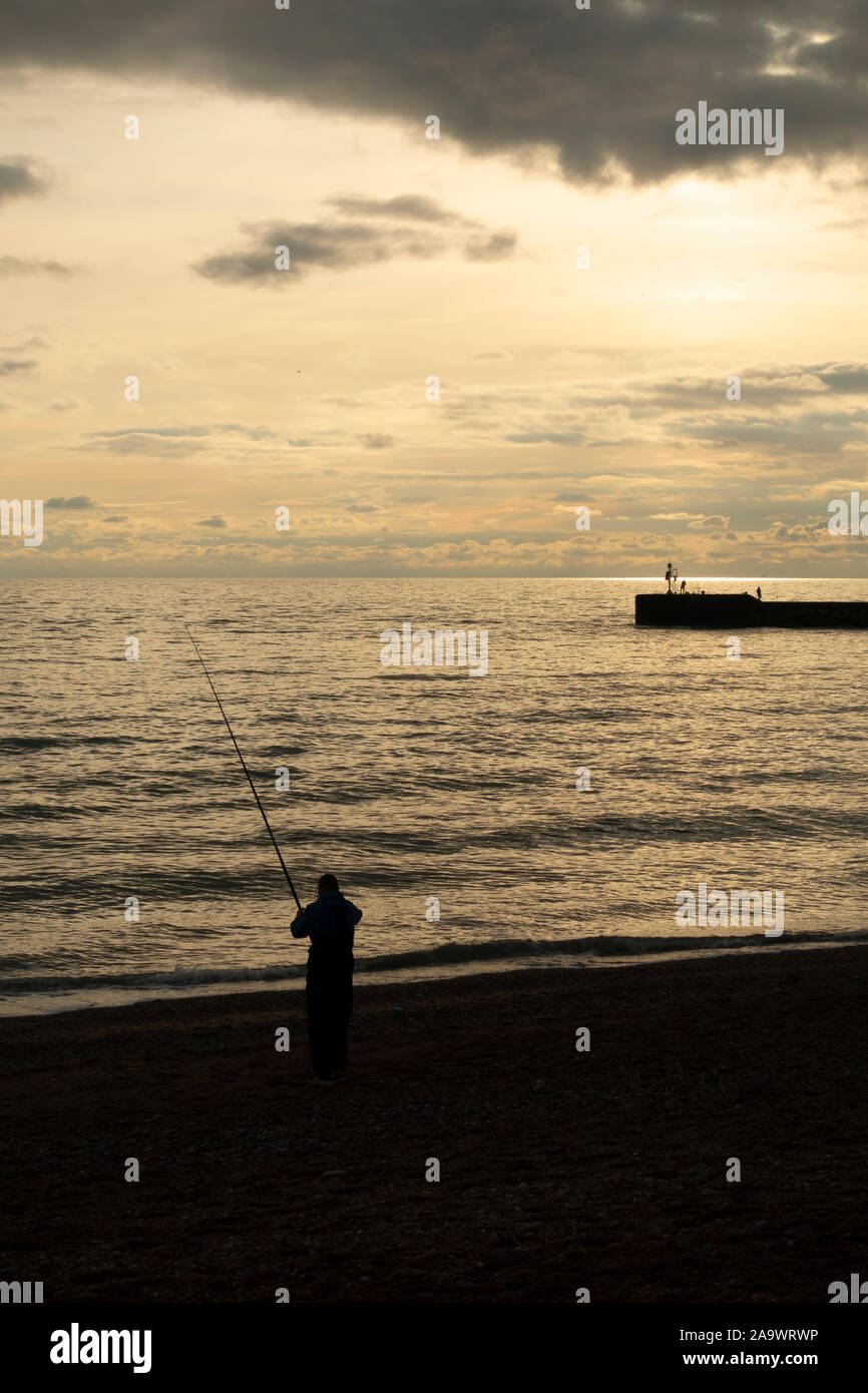Silhouette di un uomo pesca in mare sulla spiaggia di Hastings. Hastings, East Sussex, Inghilterra Foto Stock