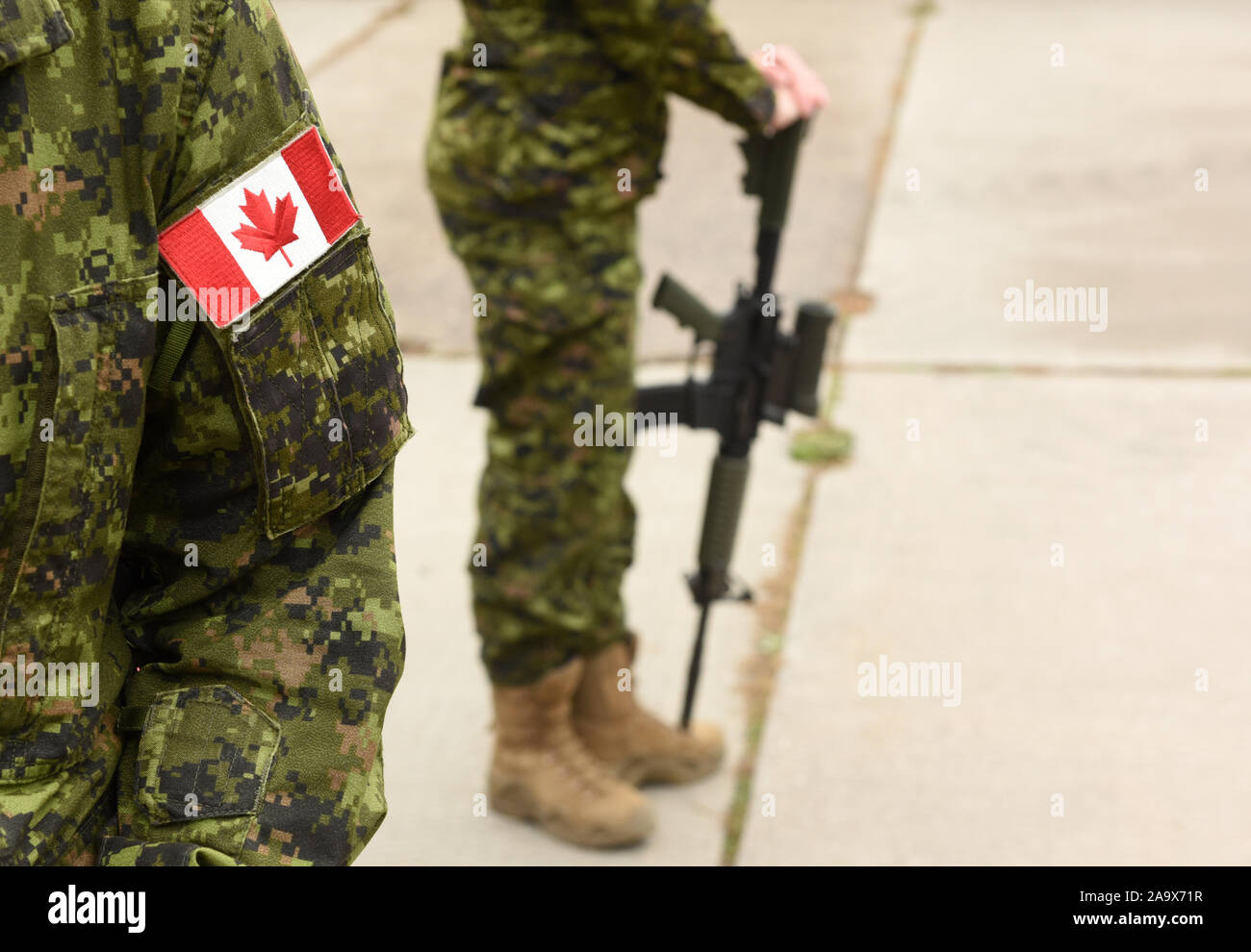 Bandiera del Canada in uniforme militare e soldato con arma sullo sfondo. Soldati canadesi. Esercito canadese. Giorno del Ricordo. Canada giorno. Foto Stock