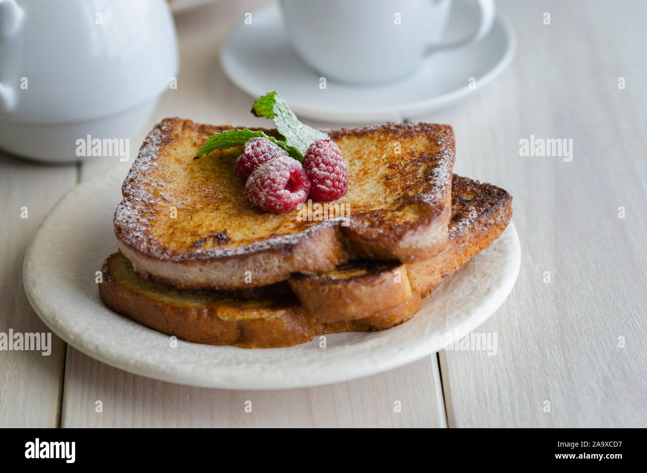 Toast alla francese, rendendo con pane ammollato nel settore delle uova e del latte, quindi fritte. Popolare piatto dolce serviti decorata con zucchero a velo e bacche servita con tazza Foto Stock