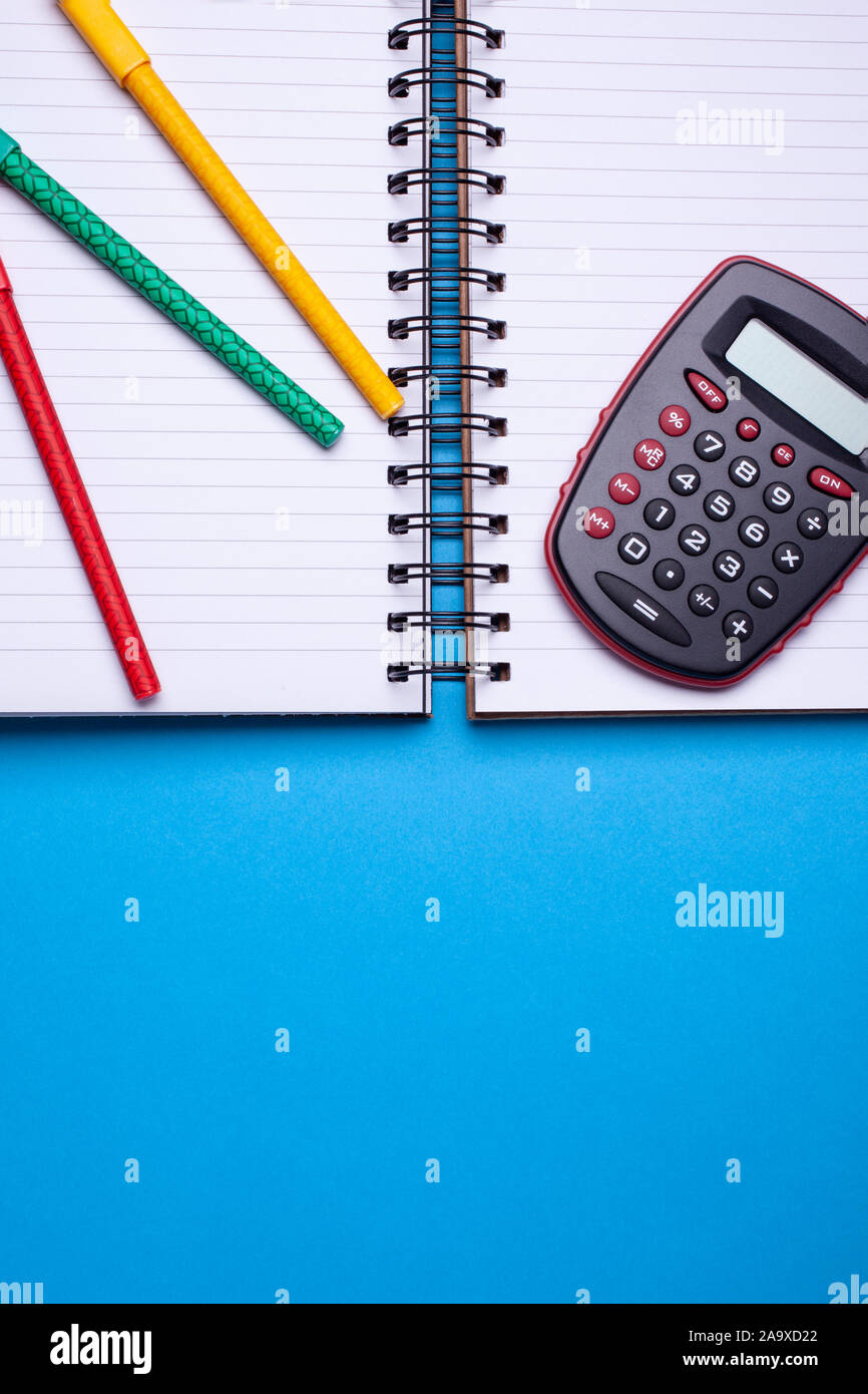 Laici flat top view mockup foto di spazio lavoro con calcolatrice tascabile, penne e copybook blu su sfondo color pastello. Foto Stock