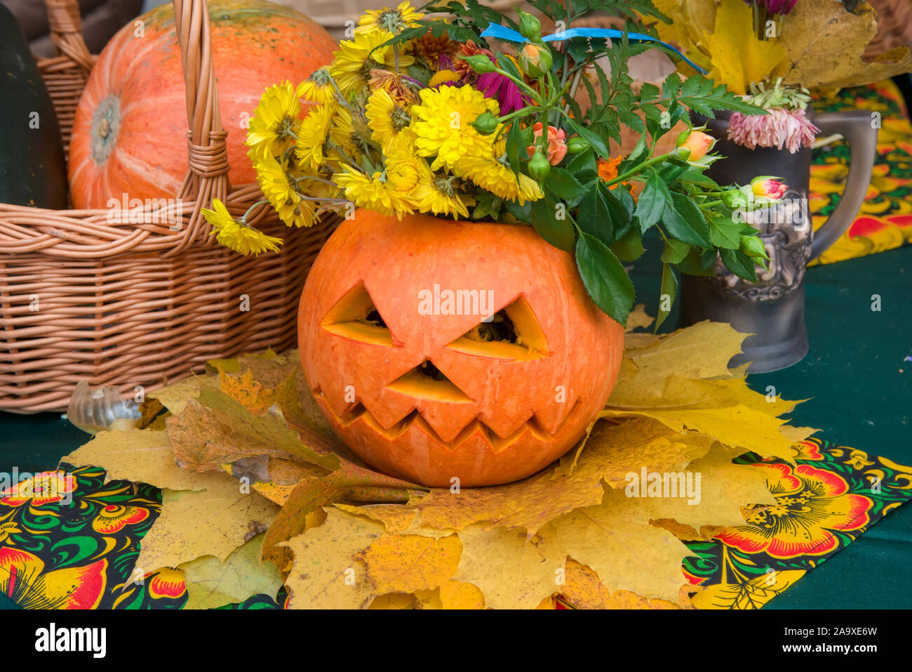 Autunno ancora in vita. La zucca con un pauroso volto scolpito su di esso con l'autunno fiori e foglie Foto Stock