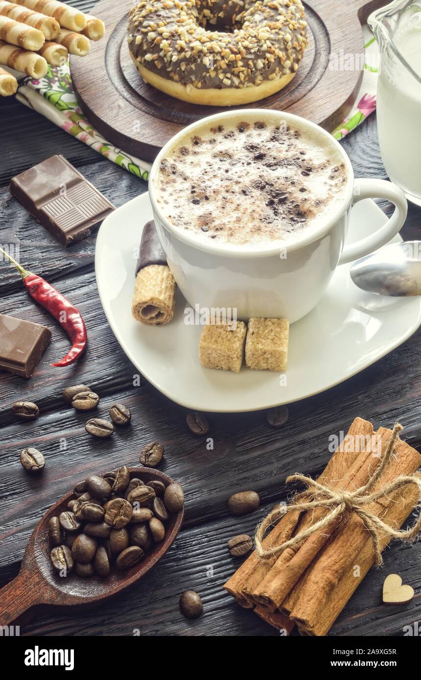 Concetto elegante di servire il caffè in stile vintage. Il caffè con la schiuma e la cannella con vari dolci e decorazione. Foto Stock