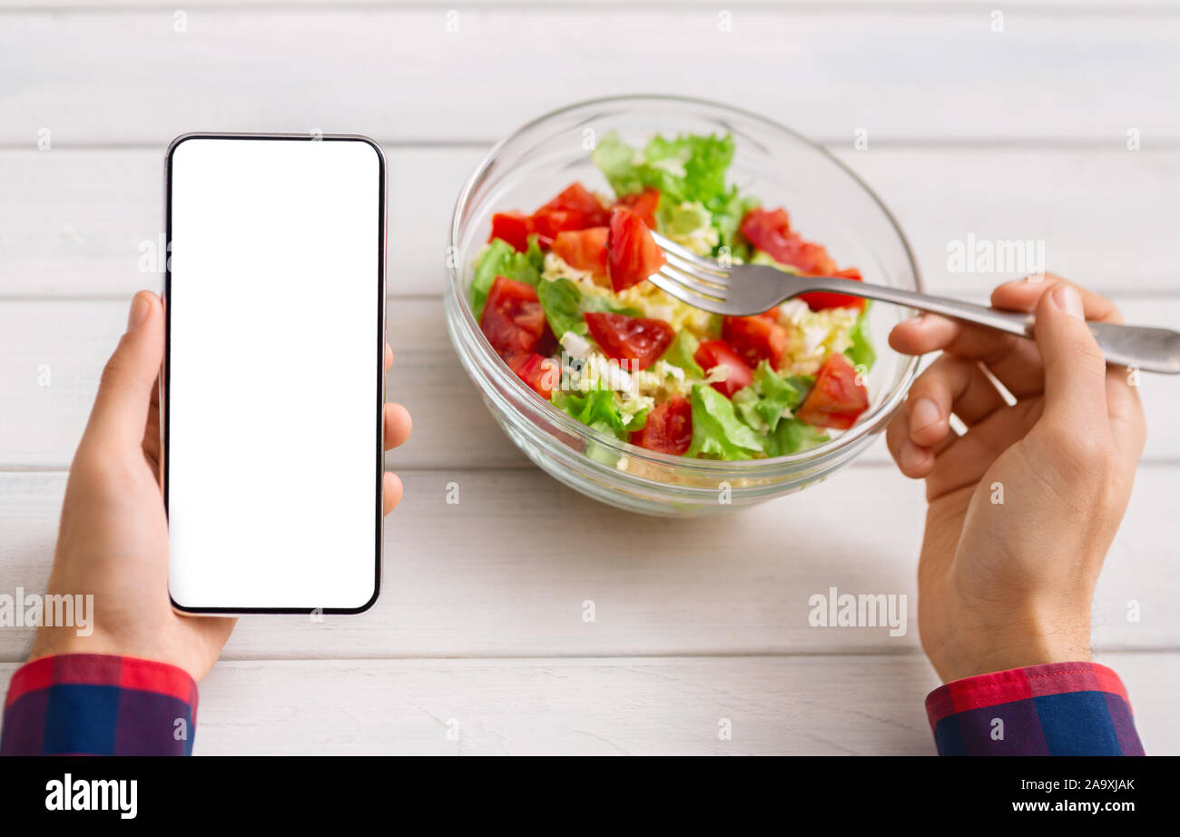 L'uomo utilizza lo smartphone con lo schermo è vuoto e mangiare insalata fresca Foto Stock