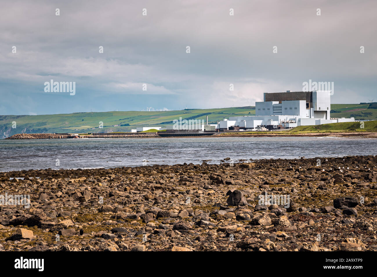 Centrale nucleare sulla costa con colline coltivate in background su un nuvoloso giorno di primavera Foto Stock