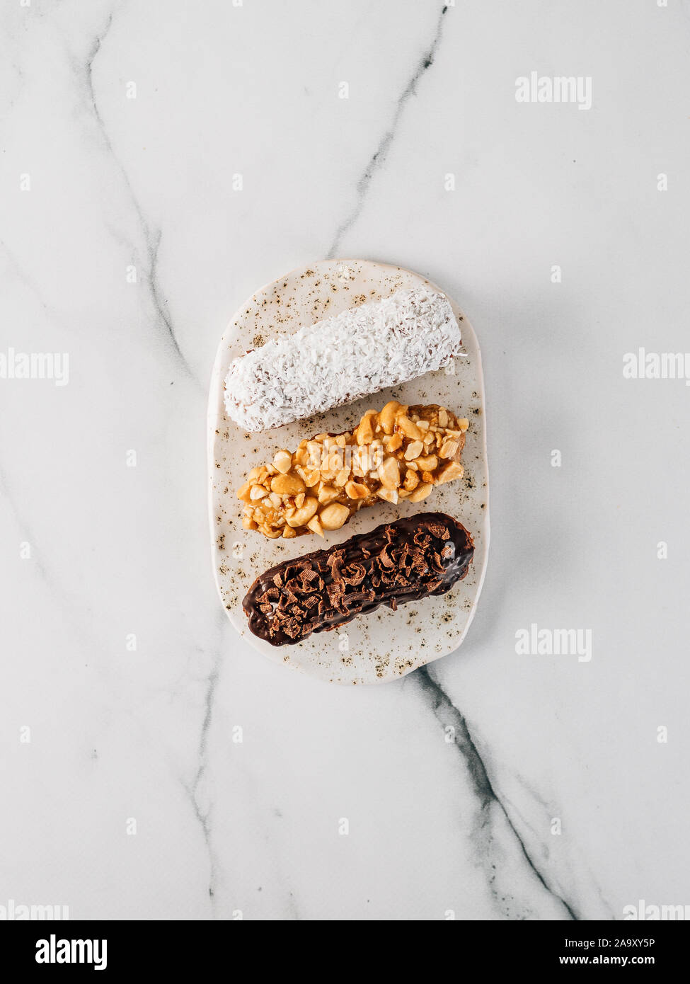 Set di tre eclairs fatti in casa su sfondo marmo. Vista superiore della deliziosa profitroles sani con decorazioni differenti elementi - cioccolato, arachidi e noci di cocco sherdded. In verticale Foto Stock