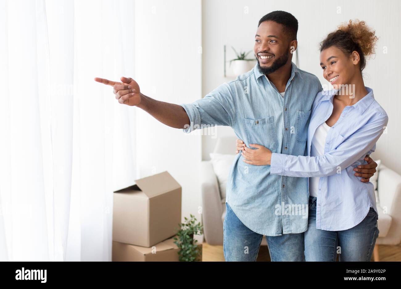 Afro marito moglie che mostra la visualizzazione della finestra abbracciando nel proprio appartamento Foto Stock