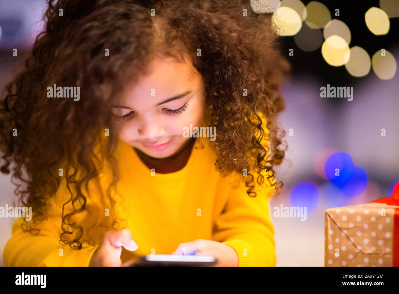 Incantevole piccola ragazza africana giocando con il telefono cellulare alla vigilia di Natale Foto Stock