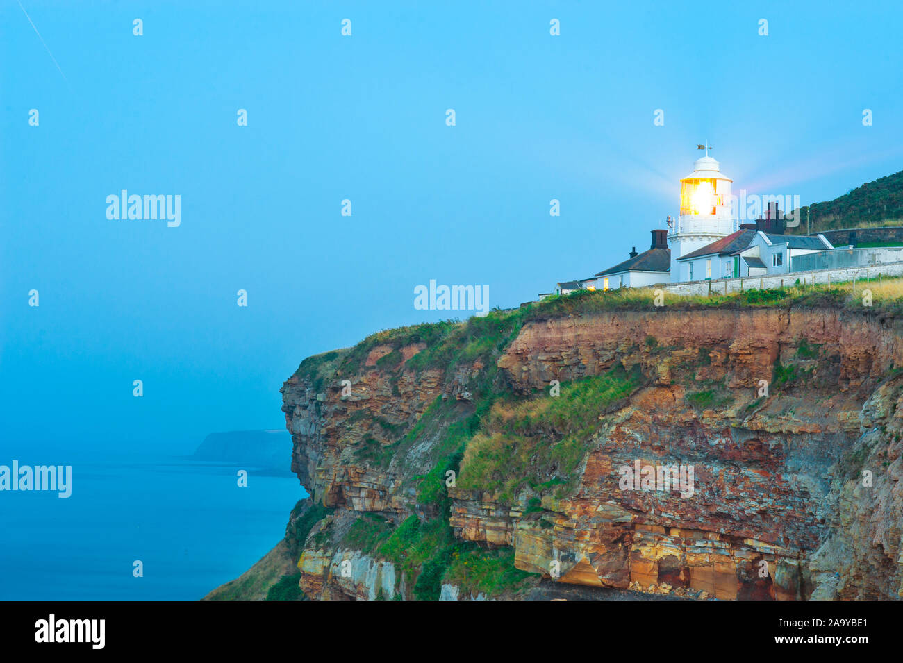 Tarda Estate opacità atmosferica al tramonto con il rock di Whitby faro. Foto Stock