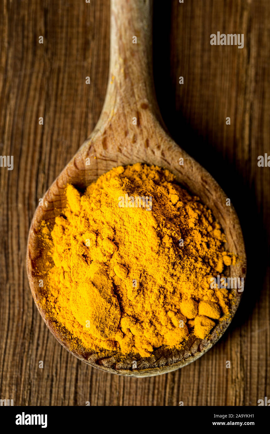 Il cucchiaio di legno con la curcuma / curcuma in polvere verticale sul tagliere di legno Foto Stock