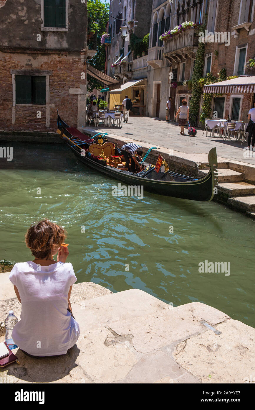 Una ragazza si siede sui passi da un canale veneziano con una gondola opposto: Rio del Megio e Calle Larga, Santa Croce, Venezia, Italia Foto Stock