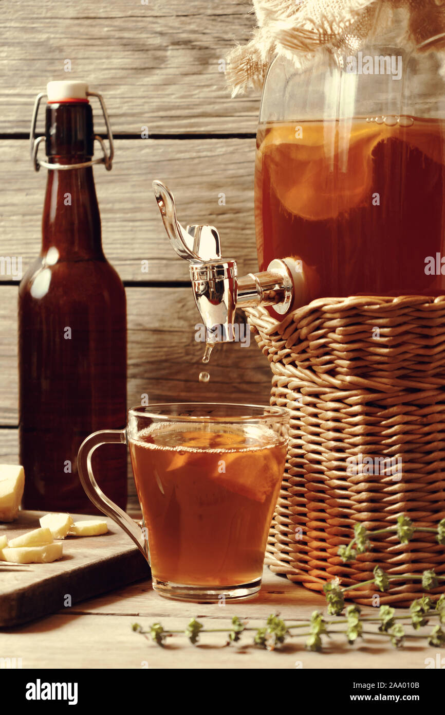 Freschi Fatti in casa il Kombucha tè fermentato drink nel vaso con rubinetto e in coppa e bottiglia su sfondo di legno, l'immagine verticale Foto Stock