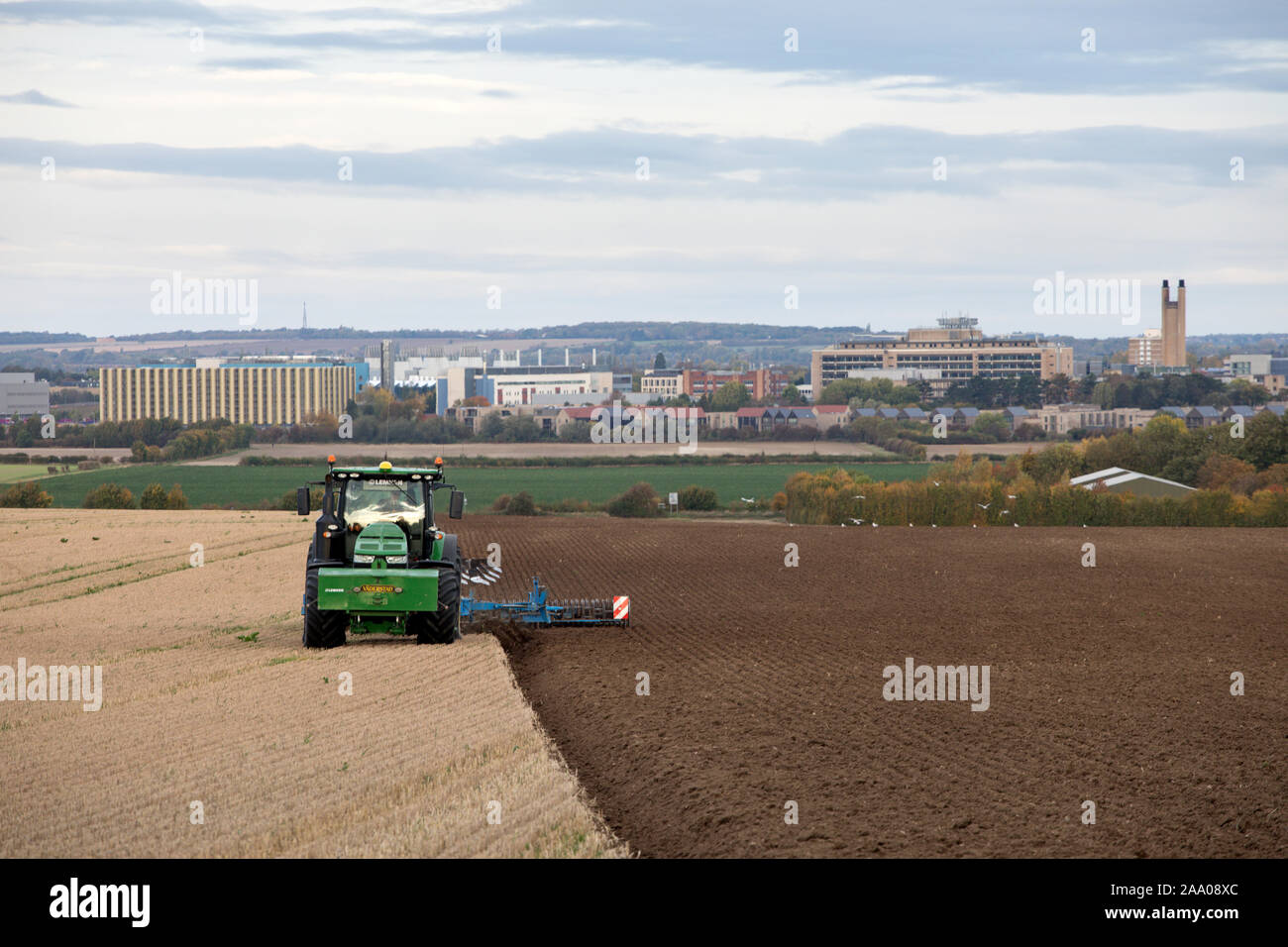 Campi di aratura dei trattori alla periferia di Cambridge con Addenbrookes ospedale in lontananza Foto Stock
