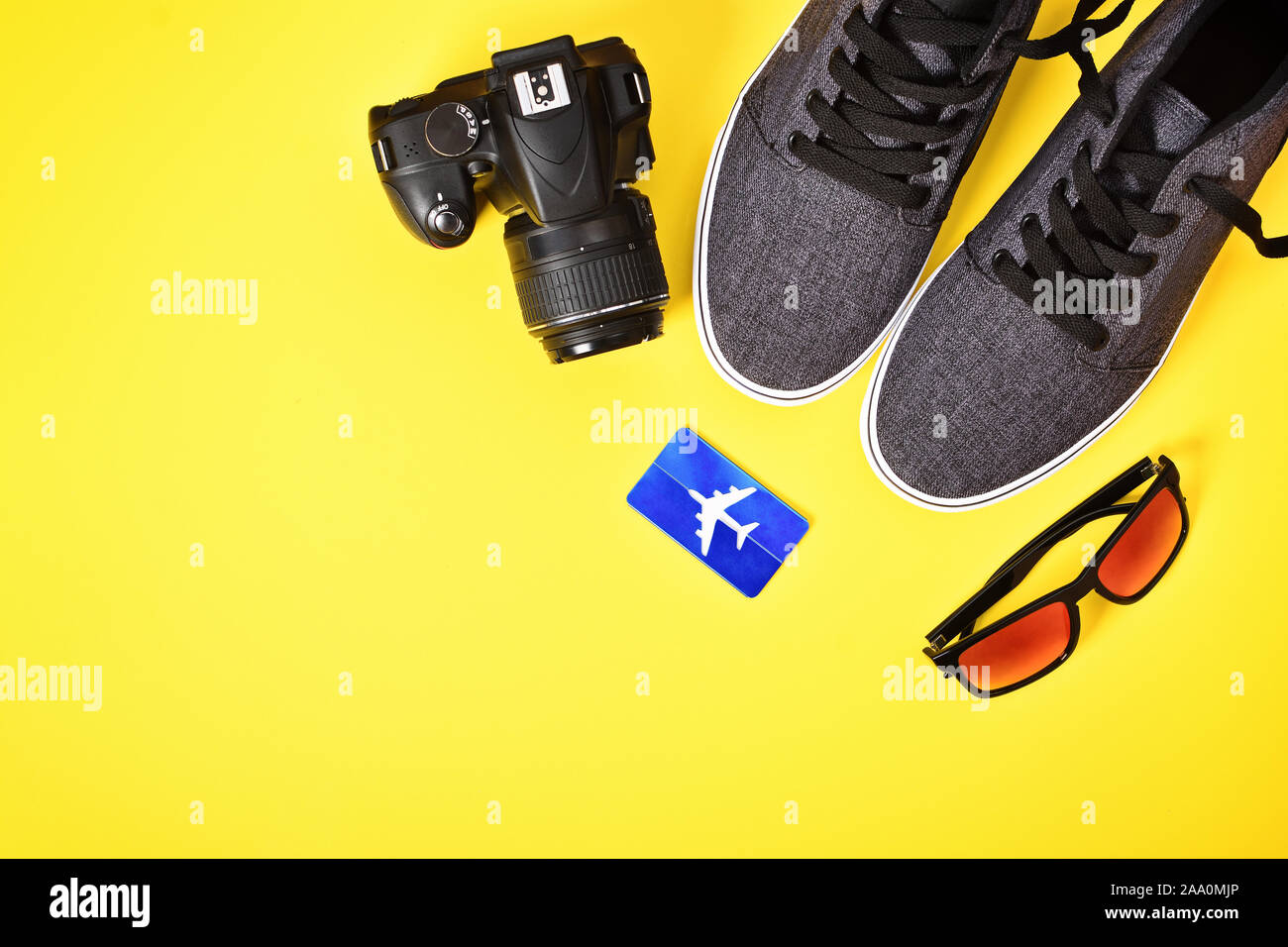 Concetto di vacanza. Vista superiore della fotocamera, aeroplano etichetta bagaglio, occhiali da sole e scarpe da ginnastica su sfondo giallo. Questi sono i miei Travel Essentials per un viaggio. Foto Stock