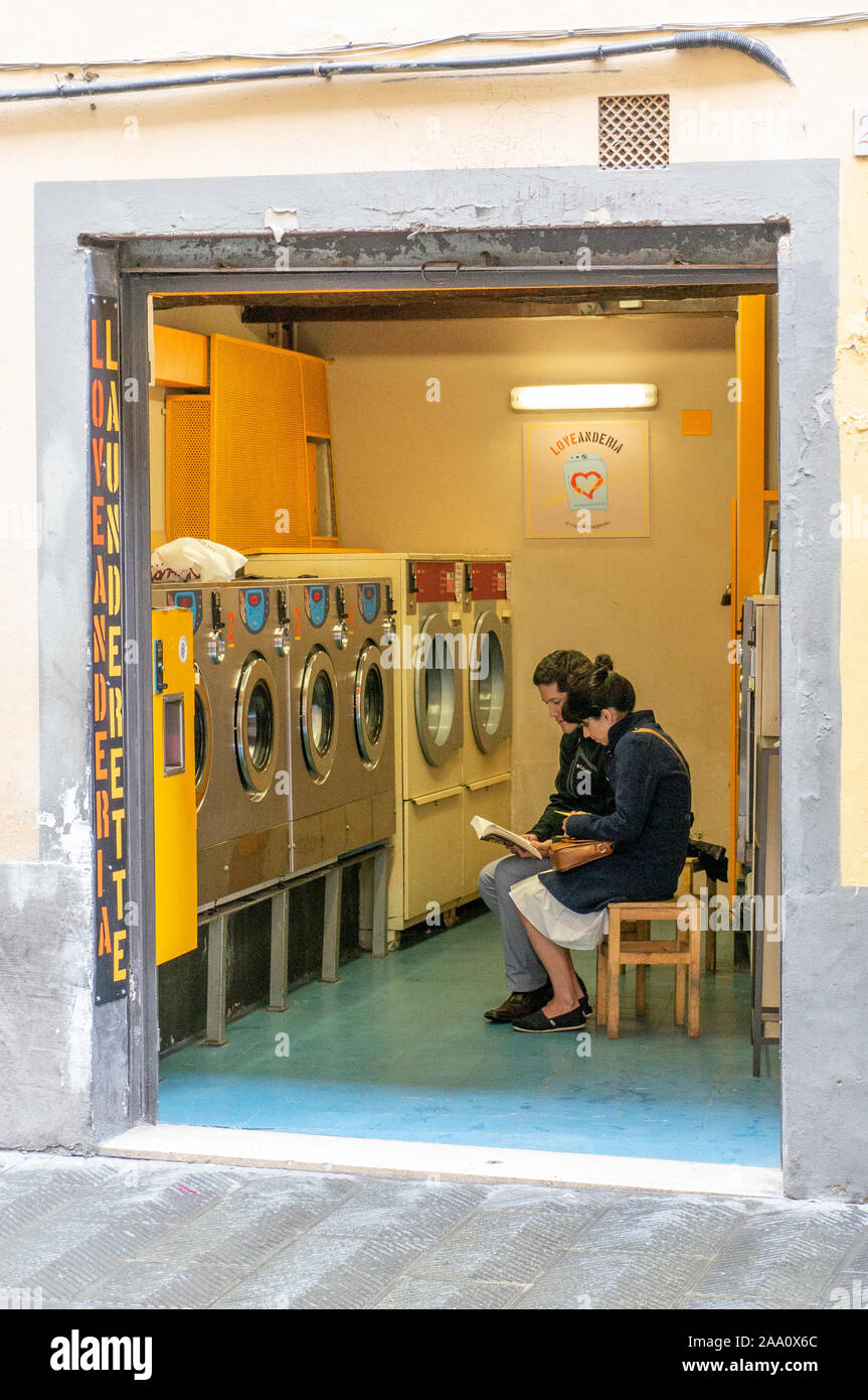 Giovane studiando durante l'attesa per la macchina di lavaggio in lavatrici a gettone, Firenze, Italia Foto Stock